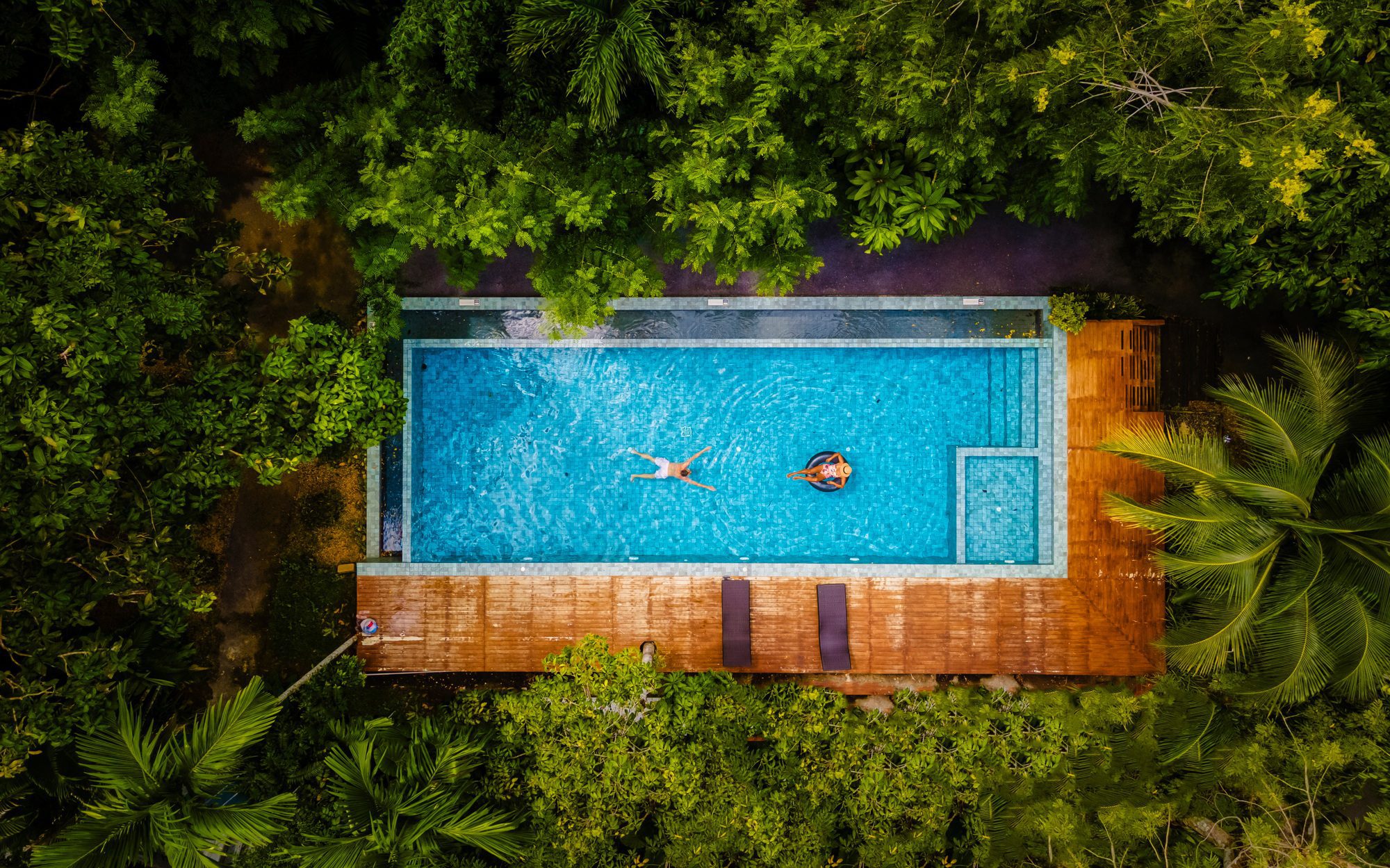 couple men and woman in swimming pool in the jungle of Krabi Thailand, aerial view with drone above