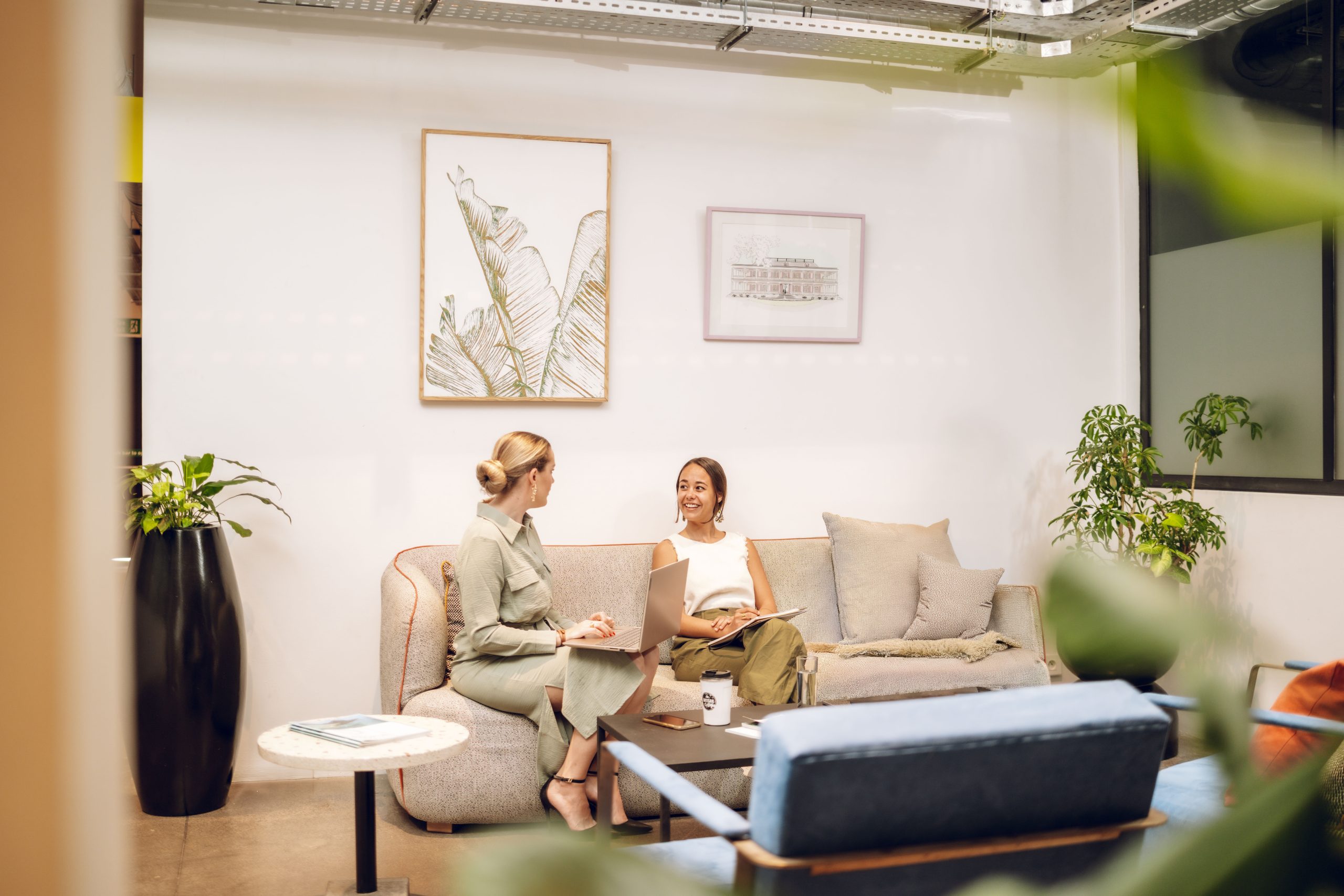 Two women discussing work in modern office lounge.